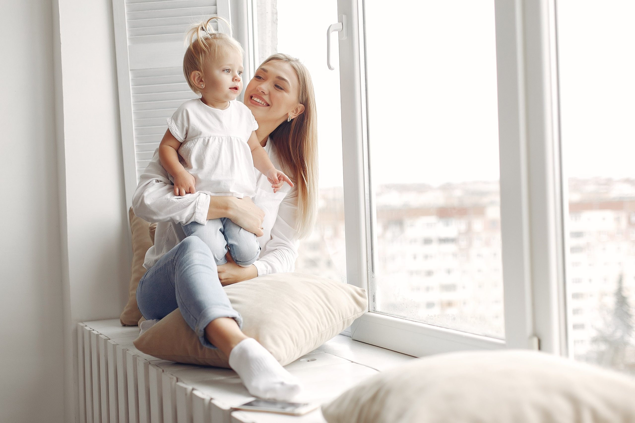 woman-holds-child-her-arms-hugs-her-mother-white-shirt-is-playing-with-her-daughter-family-has-fun-weekends-min